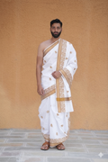 Man wearing a white dhoti with gold border against a beige background