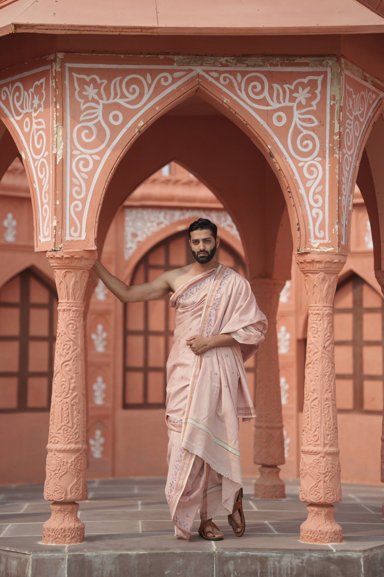 Man in a traditional outfit standing in an architectural setting with ornate columns.