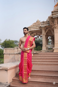 Man wearing a pink dhoti with a temple in the background