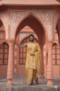 Man in traditional yellow outfit standing in a decorative architectural setting