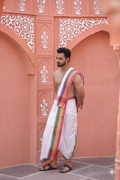 Man wearing a white dhoti with a colorful khes over his shoulder